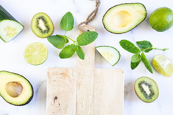 Flat lay of fresh green fruits, vegetables, and wooden cutting board