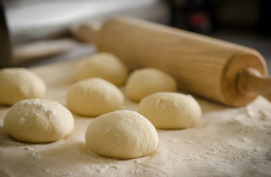 Raw dough balls and wooden rolling pin on floured surface