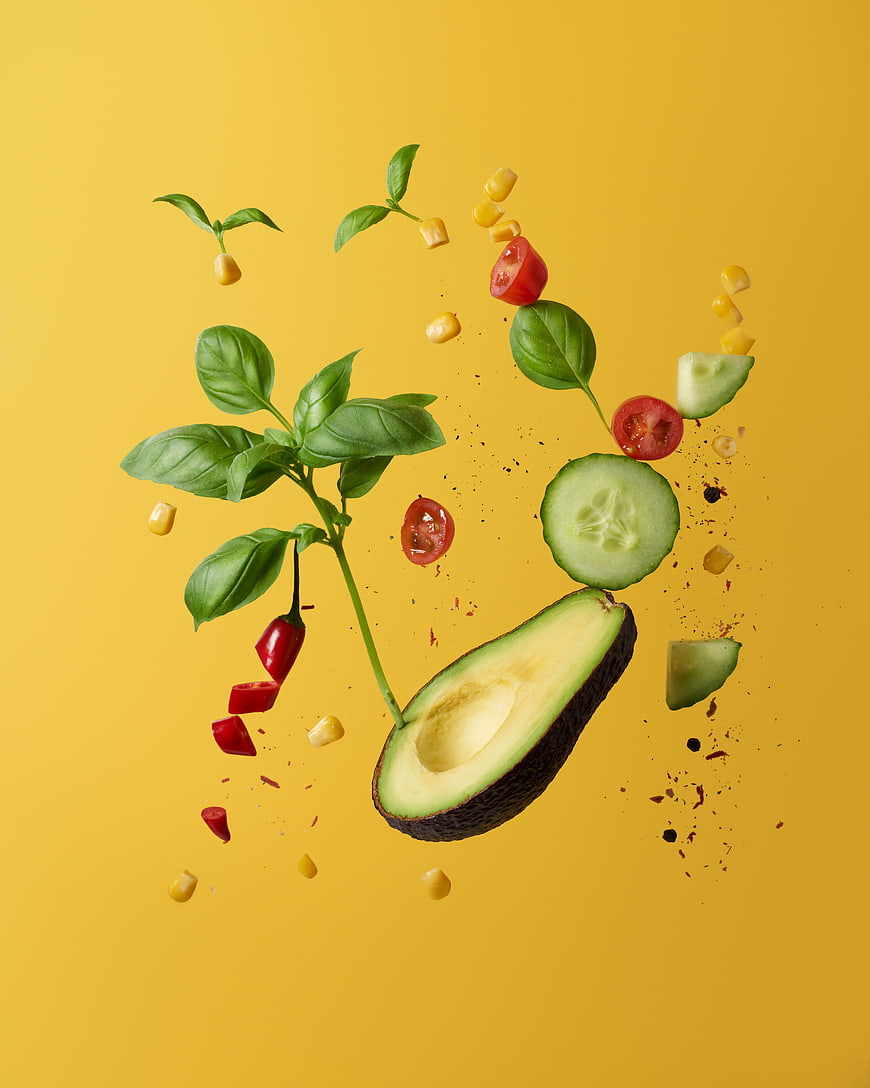 Fresh avocado, basil, and vegetables floating on yellow background