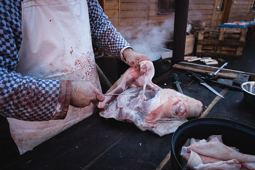 Butcher carving raw pork leg on wooden table