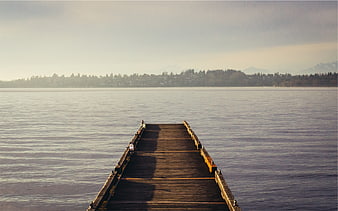 Wooden pier extending into calm lake with distant mountains