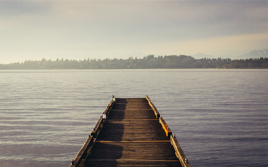 Wooden pier extending into calm lake with distant mountains