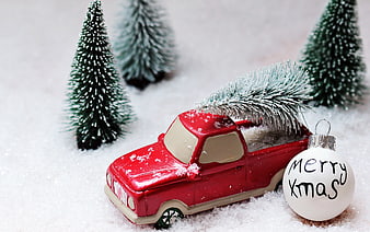 Red toy truck carrying Christmas tree in snow with ornament