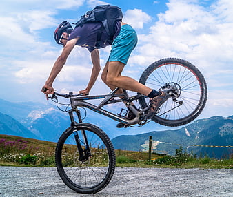 Mountain biker performing wheelie on gravel road with alpine background
