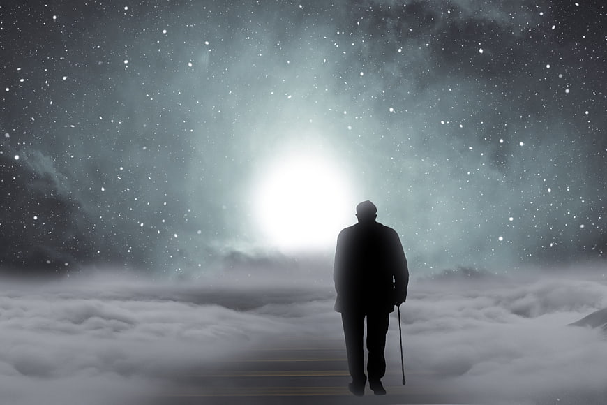 Silhouette of elderly man walking toward light in clouds