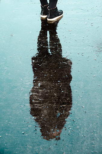 Woman's reflection in icy puddle wearing black sneakers