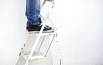 Person standing on paint-splattered ladder against white wall
