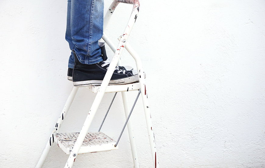 Person standing on paint-splattered ladder against white wall