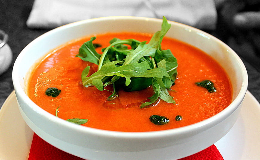Creamy tomato soup with fresh arugula garnish in white bowl