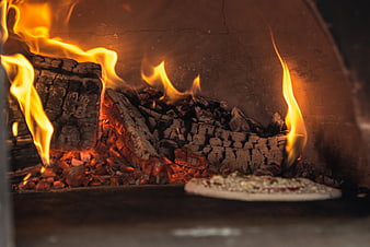 Wood-fired pizza baking in a rustic brick oven with flames
