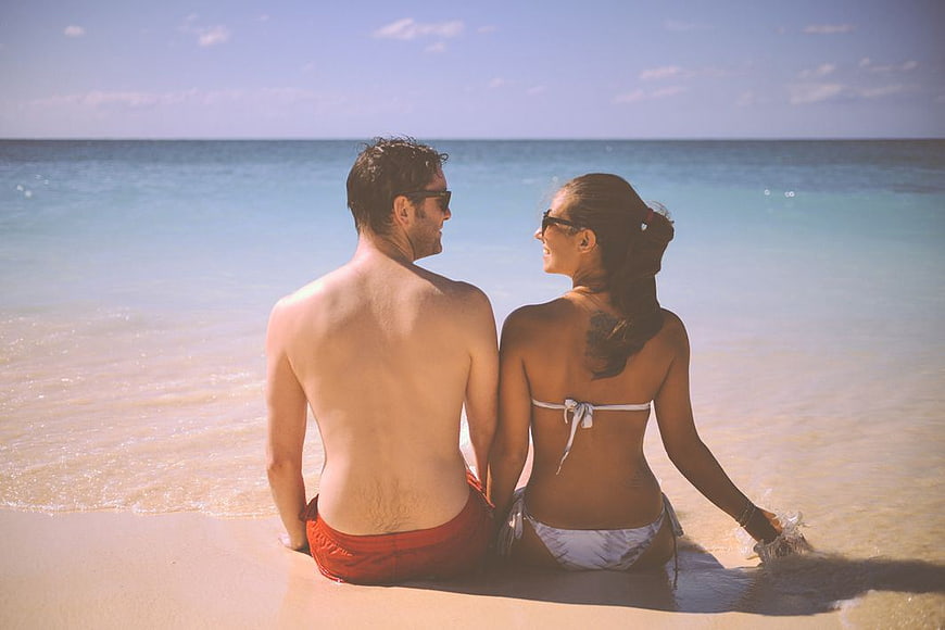 Happy Couple Sitting on Tropical Beach Looking at Ocean