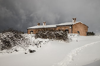 Snow-covered rustic building on a hillside under stormy sky