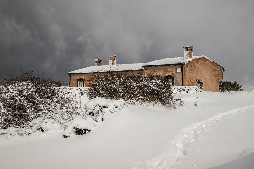 Snow-covered rustic building on a hillside under stormy sky
