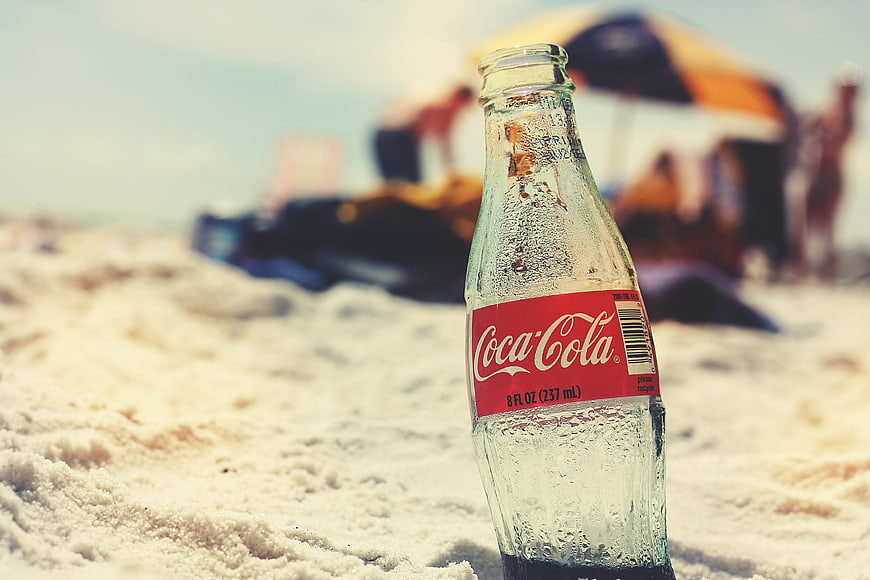 Coca-Cola glass bottle on sandy beach with blurred background