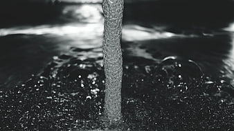 Black and white water stream splashing into dark liquid