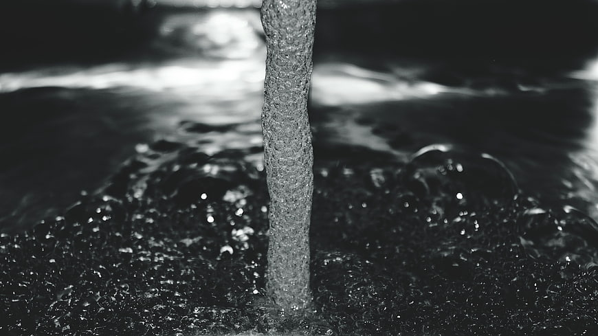 Black and white water stream splashing into dark liquid