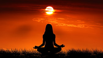 Woman meditating in lotus pose silhouette against vibrant orange sunset sky