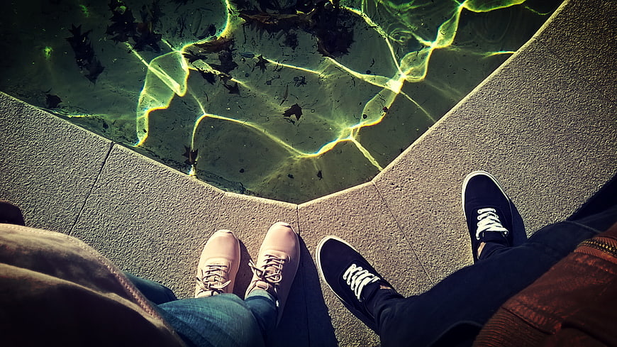 Couple's feet by pool edge with caustic light reflections