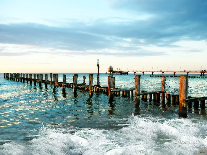 Woman standing on wooden pier in Baltic Sea at sunset