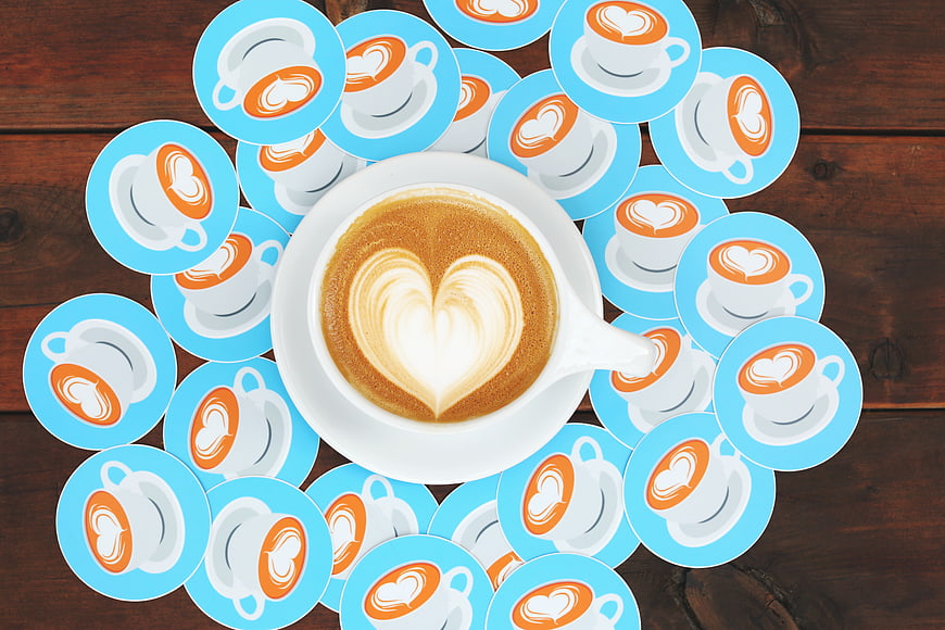 Flat lay of coffee cup with heart latte art surrounded by stickers