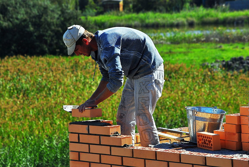Construction worker laying bricks outdoors in sunny field