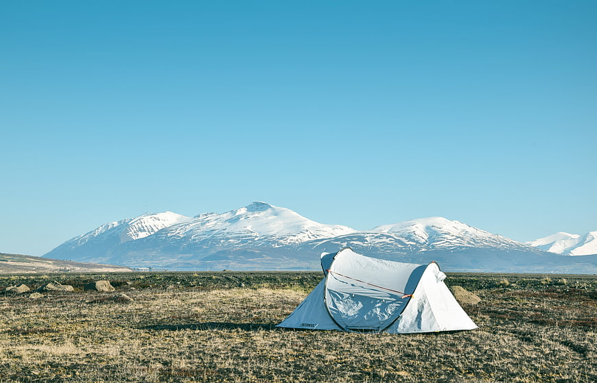 White tent camping in Icelandic landscape with snow-capped mountains