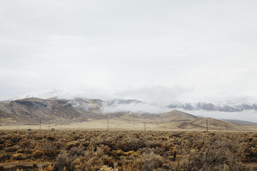 Snow-capped mountains with low clouds over arid sagebrush landscape
