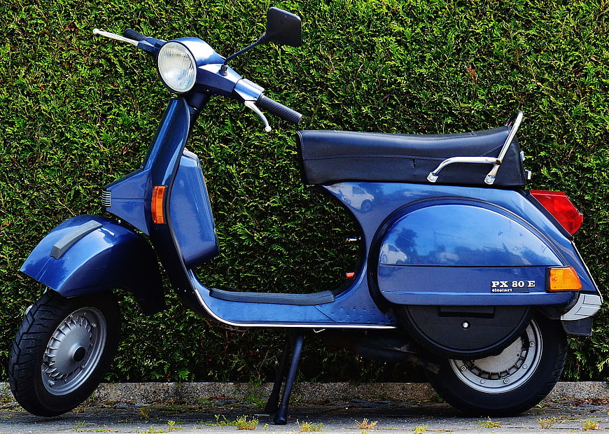 Blue Piaggio PX 80 E Scooter Parked by Green Hedge
