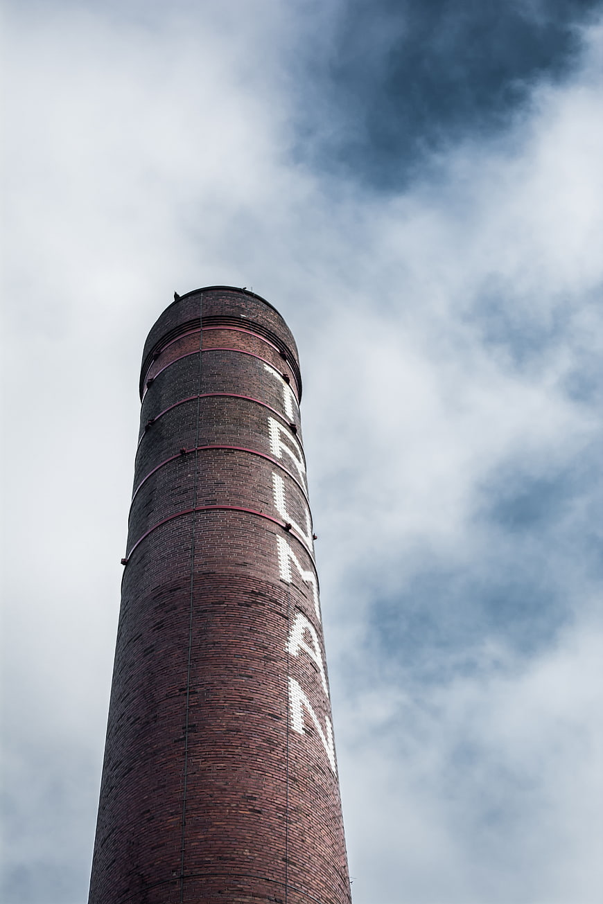 Low angle view of tall brick chimney against cloudy sky