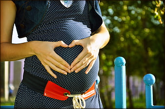 Pregnant woman making heart shape with hands on belly