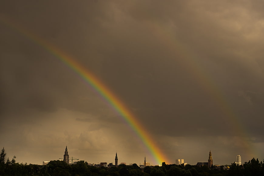 Double rainbow over city skyline with dark storm clouds