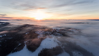 Aerial view of snowy mountain peaks above sea of clouds at sunset