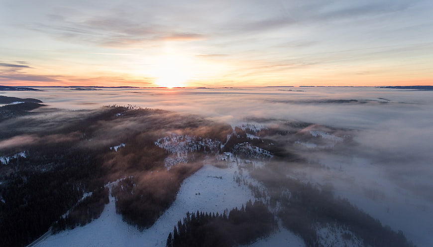 Aerial view of snowy mountain peaks above sea of clouds at sunset