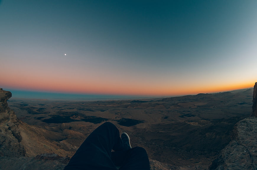 POV sitting on cliff edge overlooking desert canyon at sunset