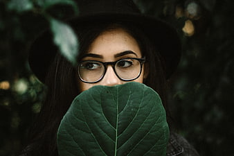 Woman with Glasses and Hat Holding Green Leaf