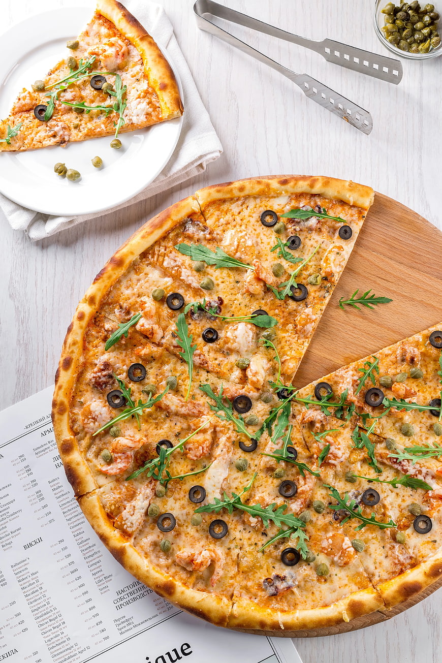 Delicious seafood pizza with olives and arugula on wooden board