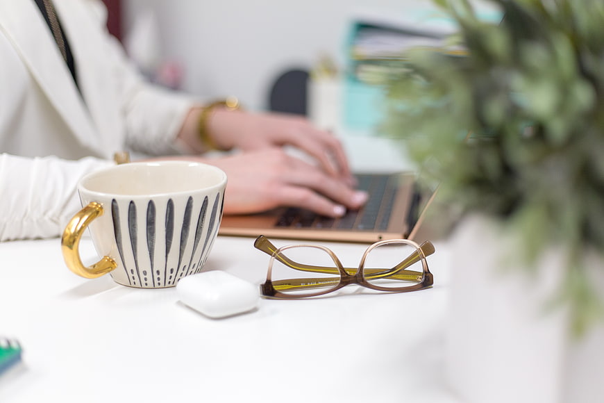 Woman typing on laptop with coffee mug and glasses on desk