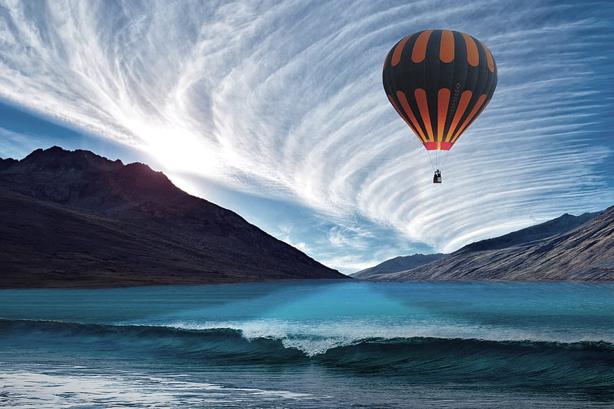 Hot Air Balloon Flying Over Turquoise Lake and Mountains