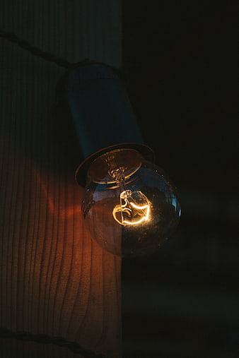 Vintage Edison Bulb Glowing Against Dark Wood Texture