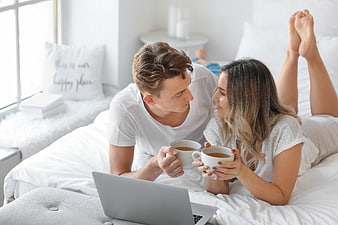Happy couple drinking coffee in bed with laptop