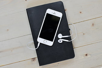 White smartphone and earbuds on black notebook on wooden table