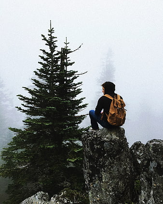 Hiker with backpack sitting on rocky peak in foggy forest