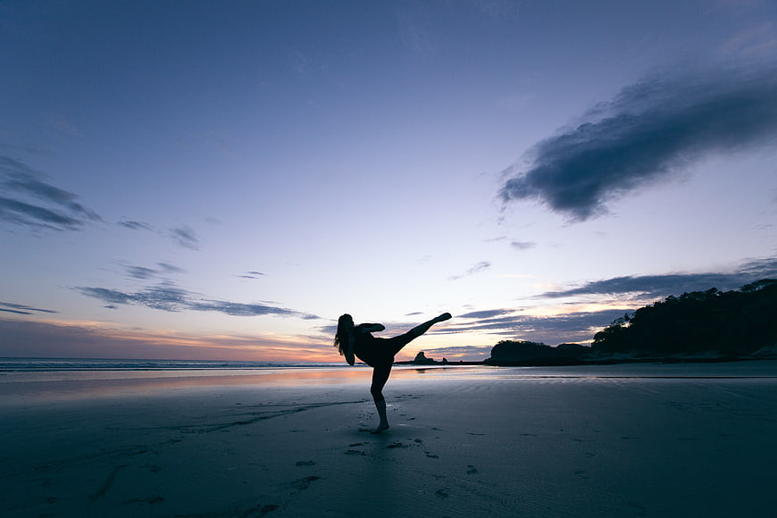 Silhouette of woman kicking on beach at sunset