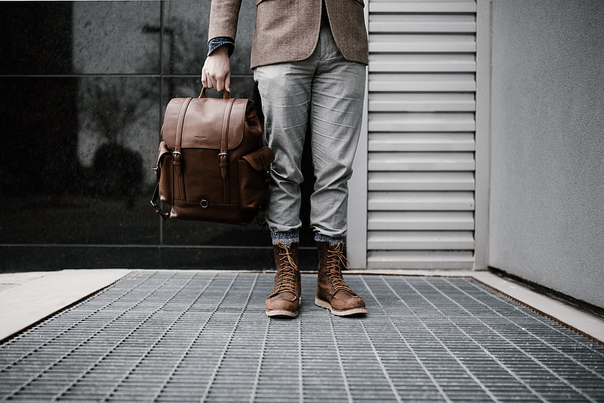 Man with brown leather backpack and boots standing on metal grate
