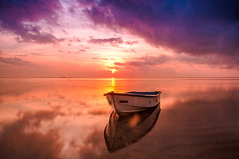 Lone boat on wet sand reflecting vibrant purple and orange sunset sky