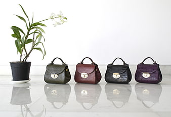 Four colorful textured handbags lined up on a reflective surface