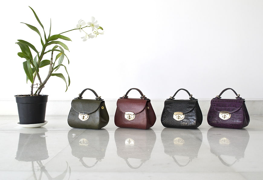 Four colorful textured handbags lined up on a reflective surface
