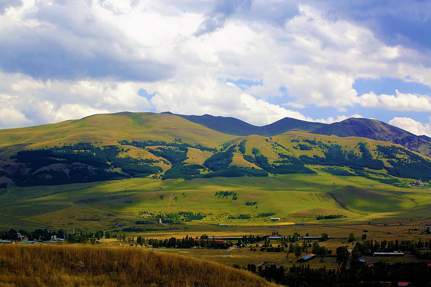 Panoramic View Of Green Rolling Hills And Mountains Under Cloudy Sky