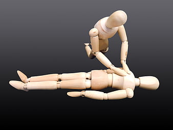 Wooden mannequins performing CPR on dark background