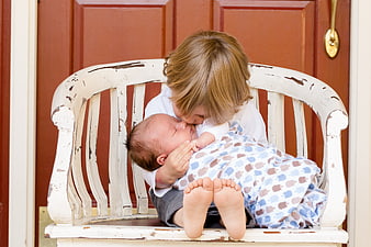 Toddler kissing newborn baby brother on rustic white bench